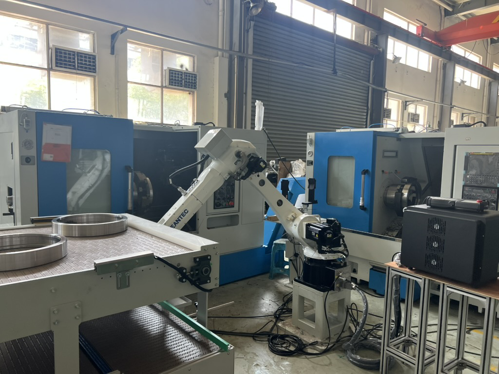Robot, machine enclosures and ring-shaped workpieces on a conveyor in a machine-tending cell